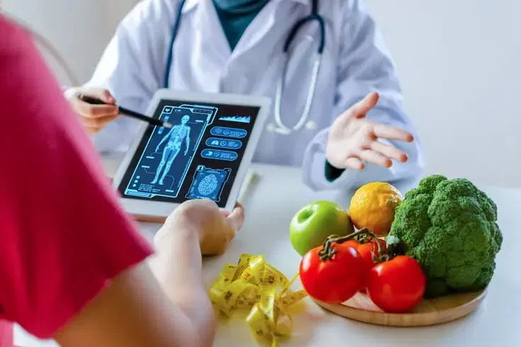 A doctor reviewing body composition results on a tablet with a patient, with fresh produce on the table