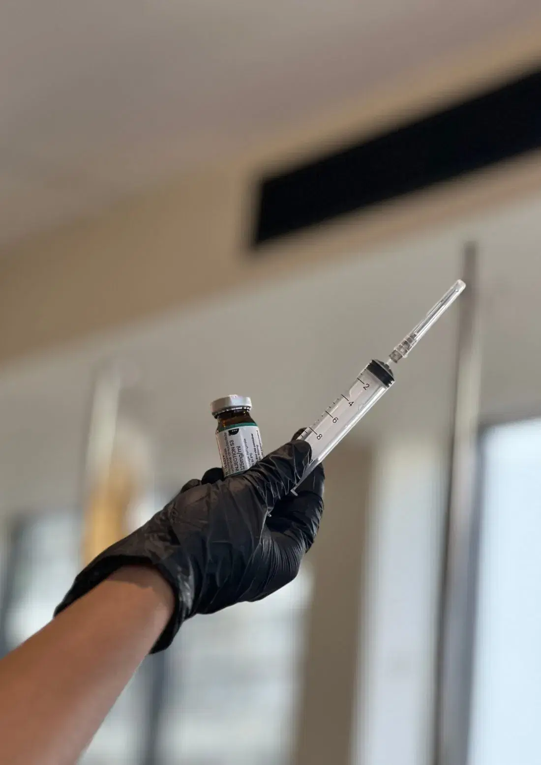 A gloved hand drawing a dose from a small vial into a syringe.