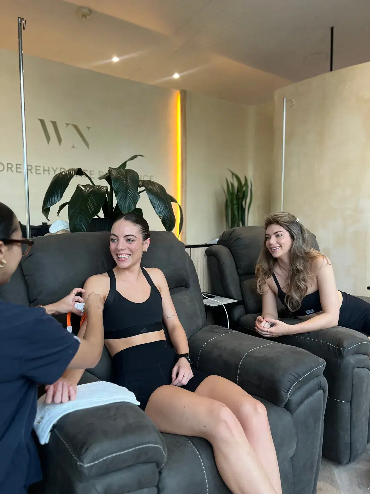 Two clients in recliners in the WellNest Gold infusion lounge, one having her IV prepared by a team member