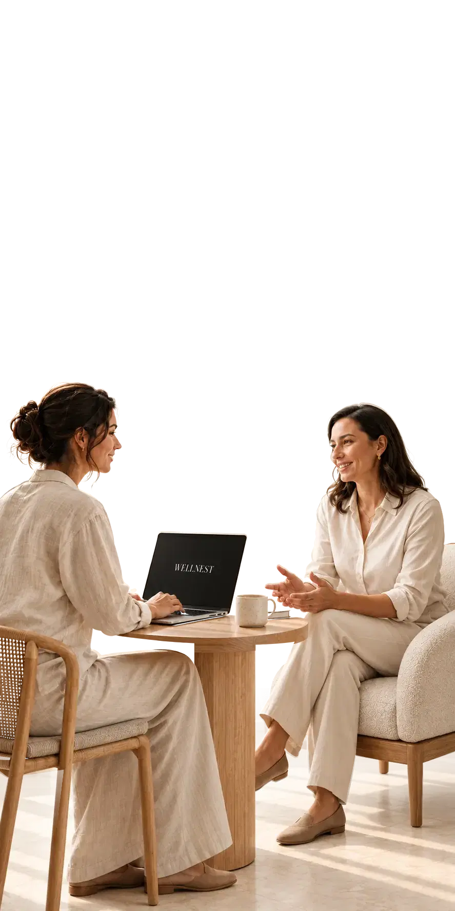 Two women in conversation at a small round table, one with a laptop showing the WellNest wordmark