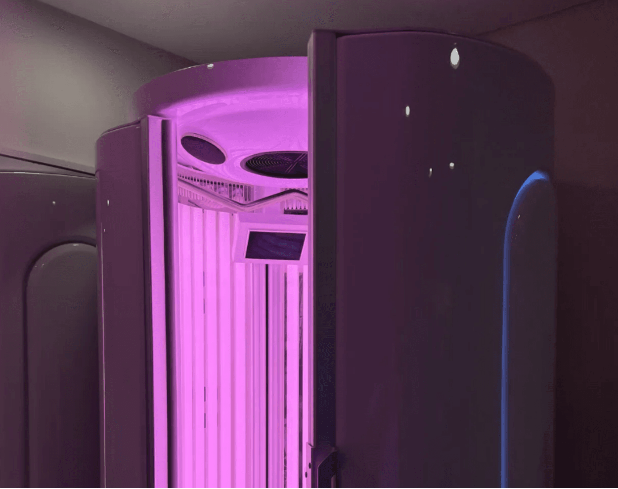A premium stand-up collagen tan can machine at WellNest in Cape Town, featuring vertical red light and low-UV bulbs emitting a bright pink glow.